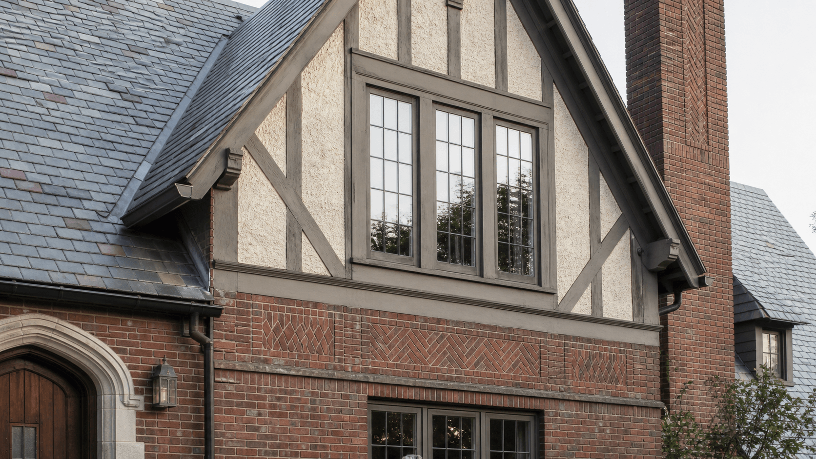 Tudor Revival 的陡山墙、装饰性半木构、stucco、花纹砖墙、窄窗和烟囱细节示意图