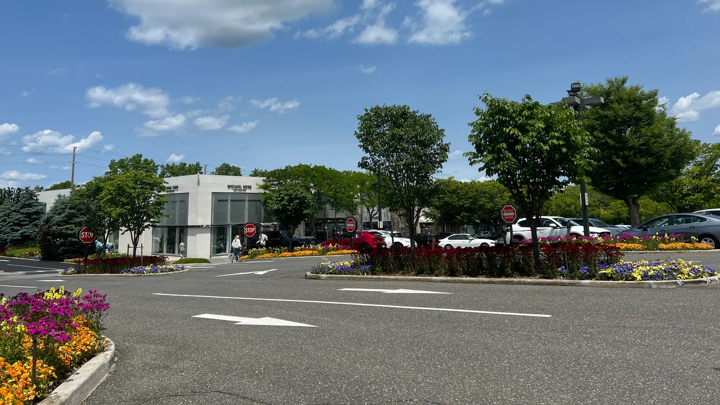Manhasset的Americana开放式购物区实拍,低层店面、停车车道与花坛,图中可见Michael Kors门店