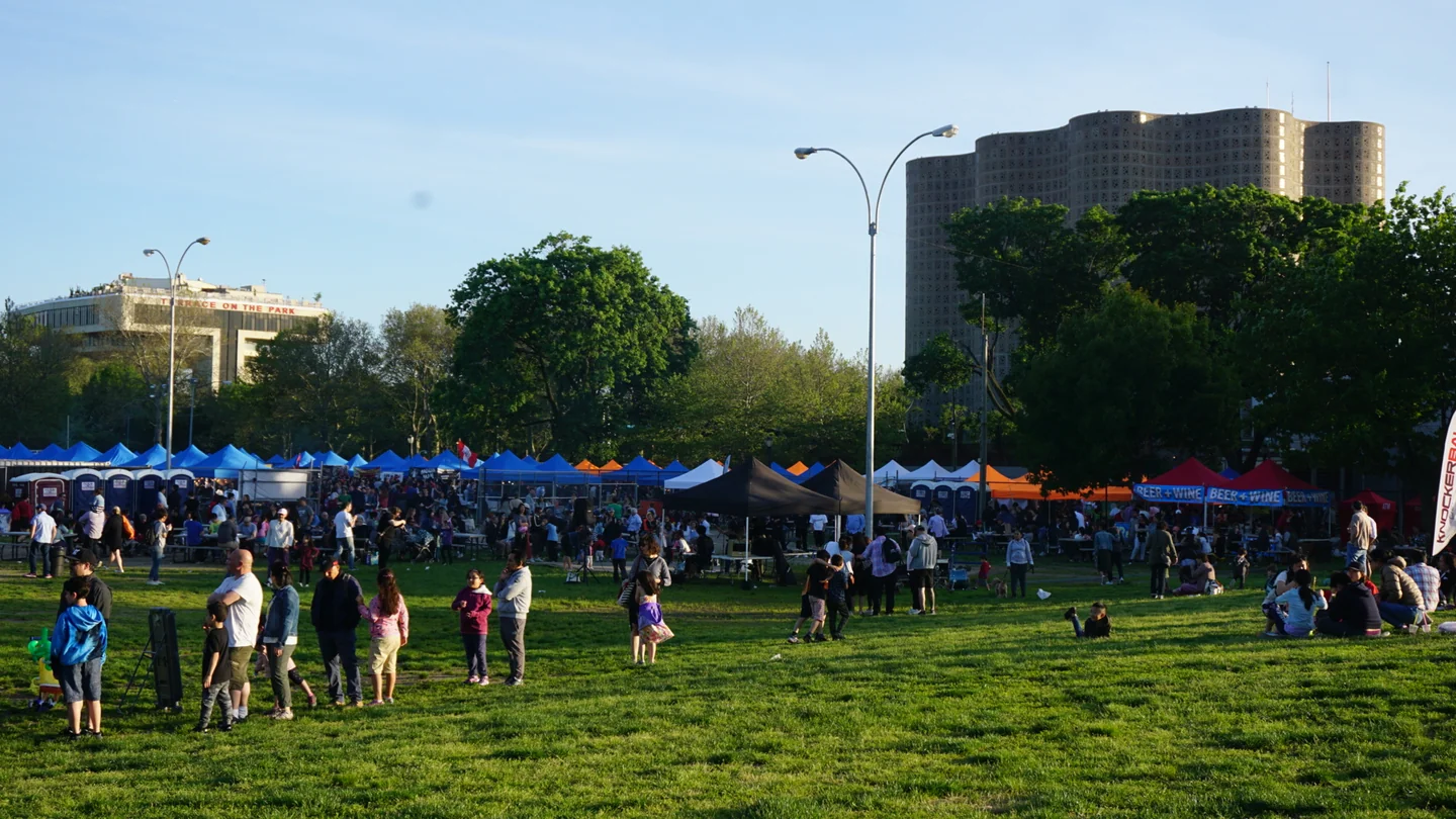 2019年5月18日，Queens Night Market 旁的草坪上有游客活动，远处可见市集摊棚